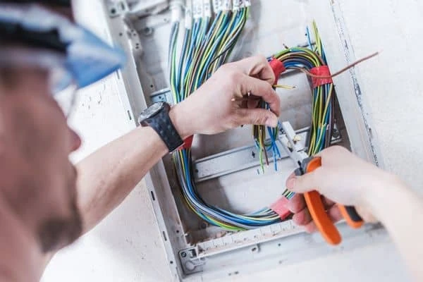 Elektrikář zapojuje dráty v rozvaděči pomocí kleští.