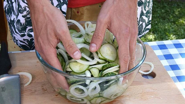 Ruce smíchají okurky a cibulku v míse