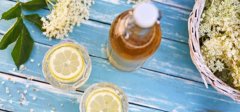 Bezová limonáda s citronem a květy bezu na modrém dřevěném stole.
