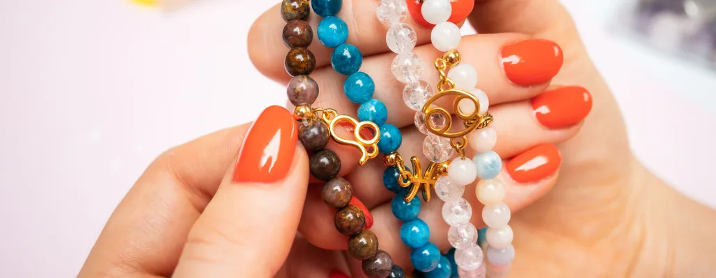 Rukou drží náramky s astrologickými znaky