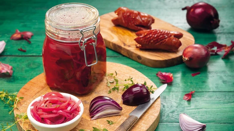 Nakládaná cibule v sklenici s čerstvou cibulí a bylinkami