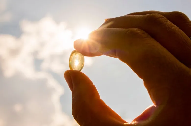 Ruka drží vitamín D ve kapsli před sluncem