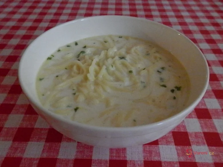 Mléková polévka s nudlemi v bílé misce na pruhovaném ubrusu.