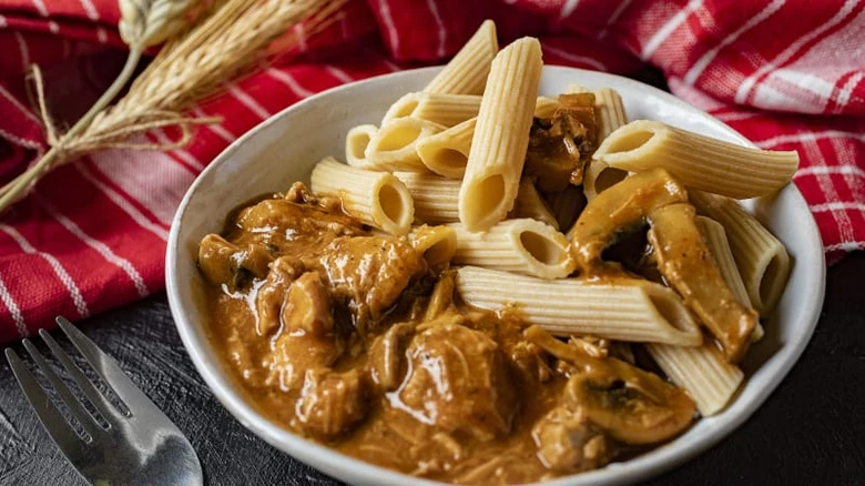 Penne s tmavou omáčkou v bílé misce na červeném ubrusu.