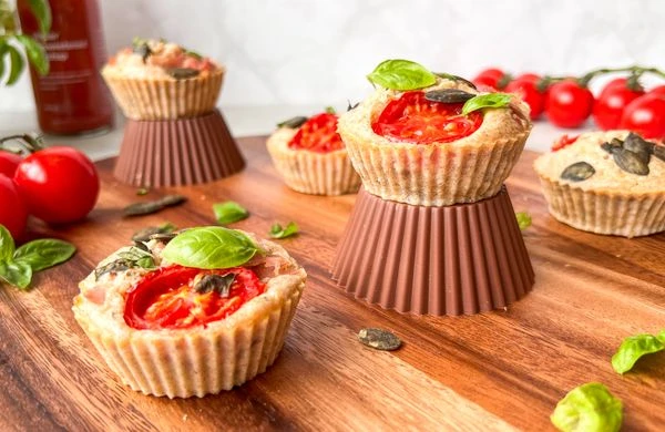 Sýrové muffiny s rajčaty a bazalkou na dřevěném podkladu.