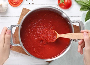 Ruční míchání rajčatové omáčky v hrnci s čerstvými ingrediencemi.