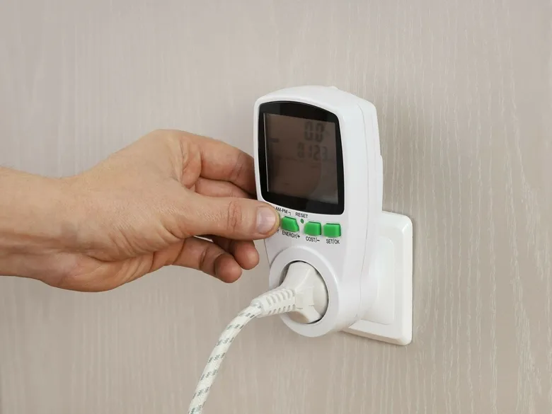Ruka nastavuje měřič spotřeby energie v zásuvce.