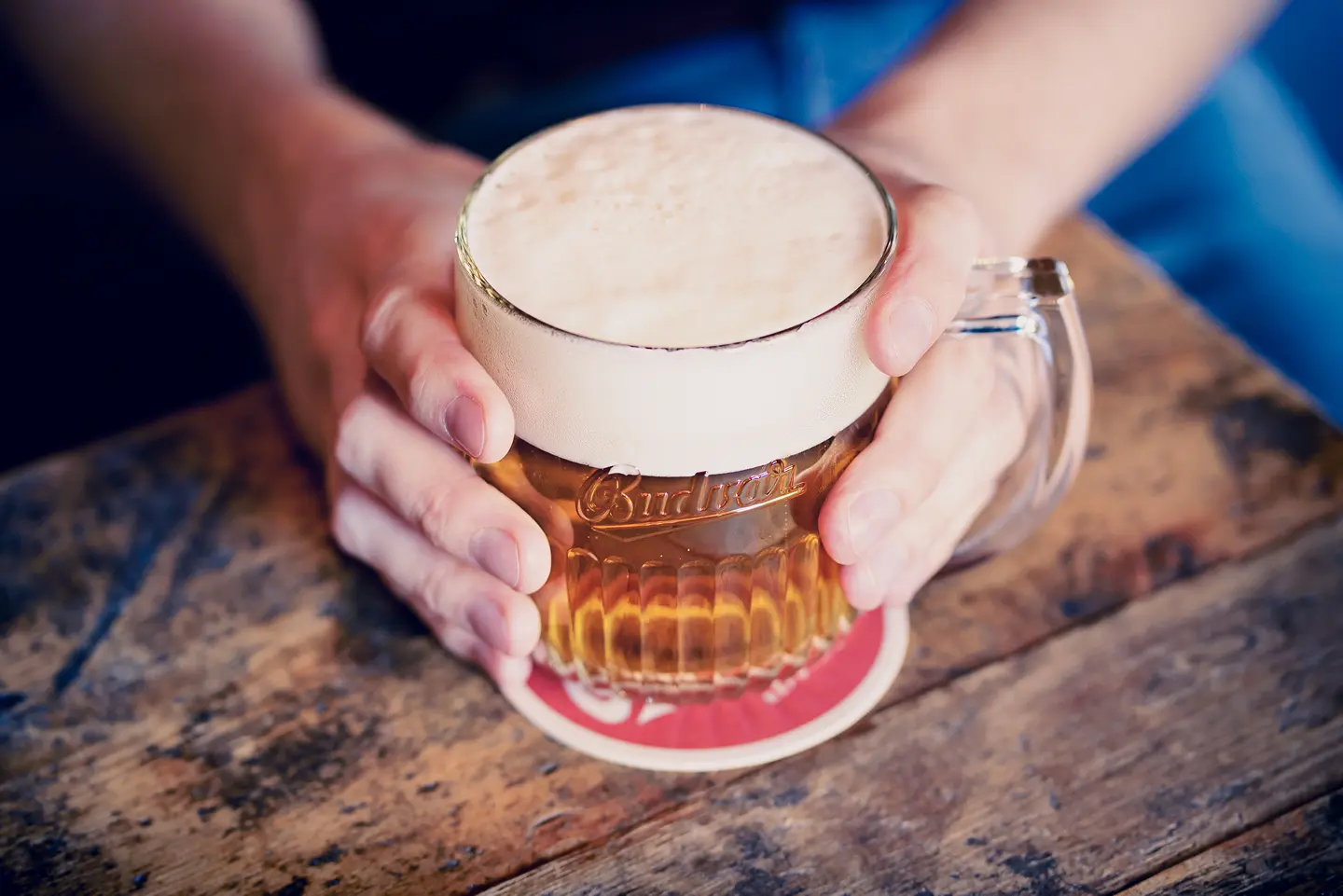 Ruka drží pivo v poháru na dřevěném stole