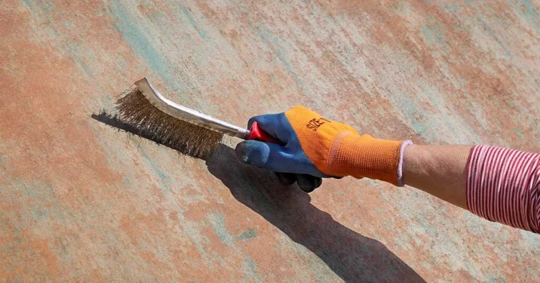 Ruka s kartáčkem odstraňuje korozi z kovu