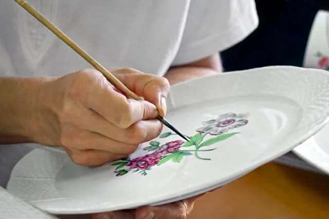 Ruka maluje květiny na porcelánový talíř