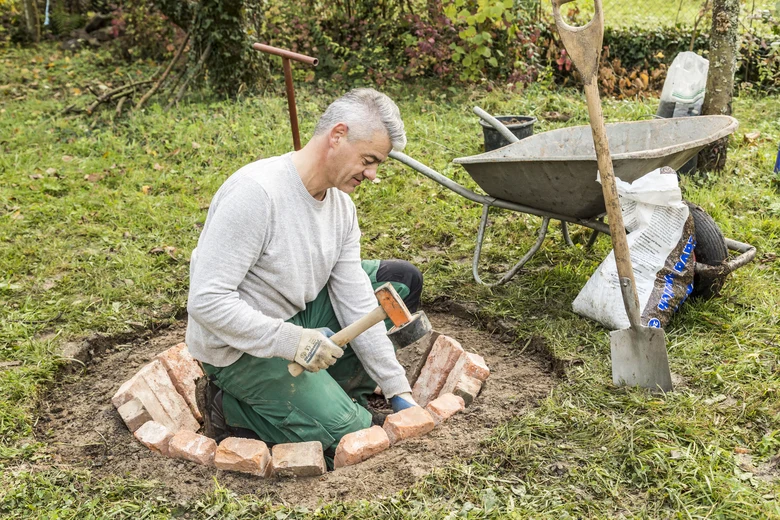 Muž staví ohniště z cihel v zahradě