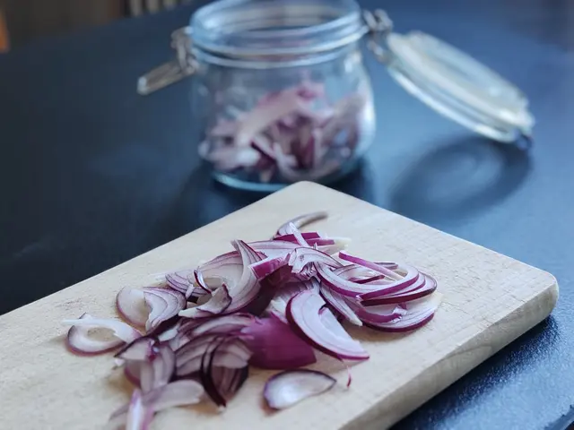 Nakrájená červená cibule na dřevěném prkénku s džbánem v pozadí.