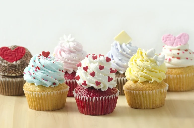 Kolorované muffiny s výzdobou na světlém dřevěném povrchu.