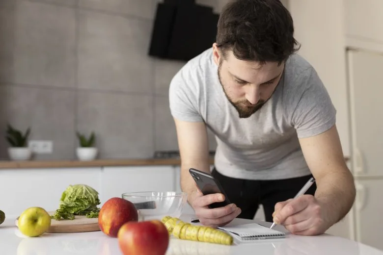 Muž počítá kalorie pomocí telefonu s ovocem na kuchyňském stole.