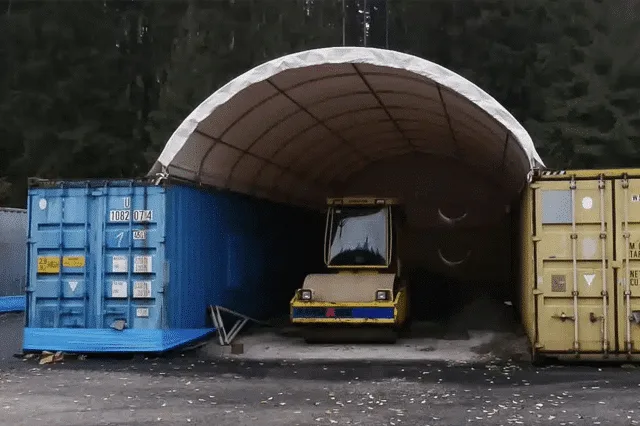 Modrý kontejner vedle žlutého pod bílým obloukem s vozem.