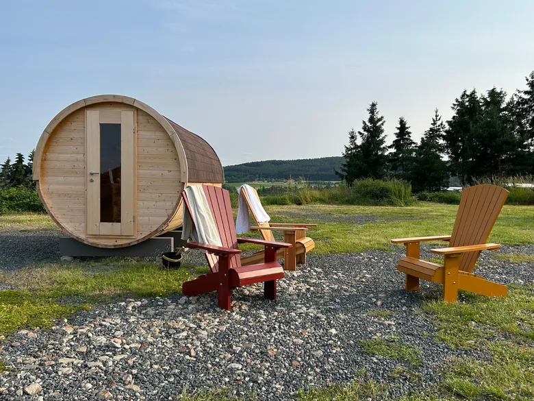 Venkovní dřevěná bubnová sauna s židlemi na štěrku.
