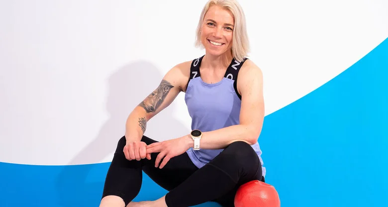 Žena v sportovním oblečení sedí vedle červeného cvičicího míče.