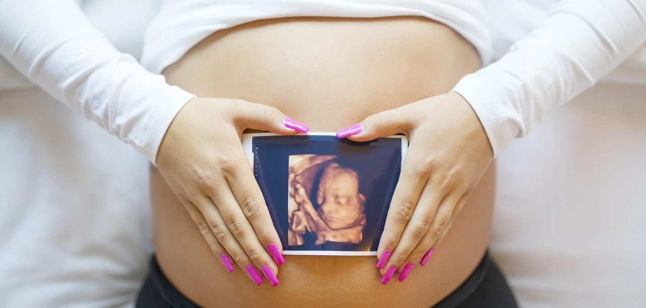 Těhotná žena drží v rukou snímek ultrazvuku na břiše.