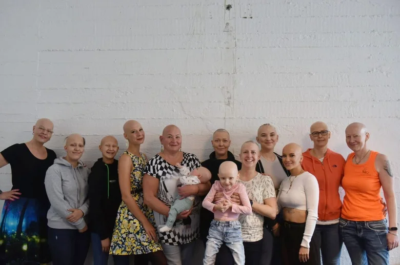 Skupina žen s alopecií se usmívá před bílou zdí.