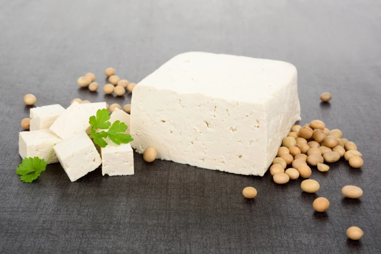 Blok tofu se kousky, sójové boby a petržel na tmavém povrchu.