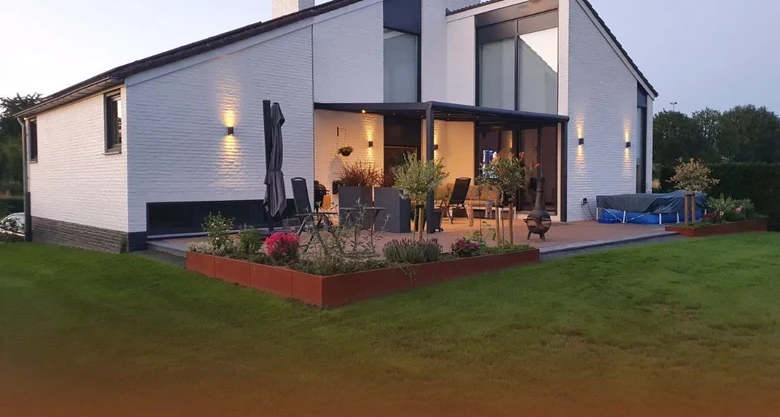 Moderní zahradní design s terasou, květinami a venkovním nábytkem u domu.