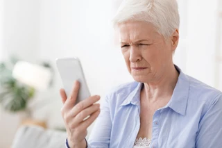 Starší žena se dívá na telefon kvůli problémům s viděním.