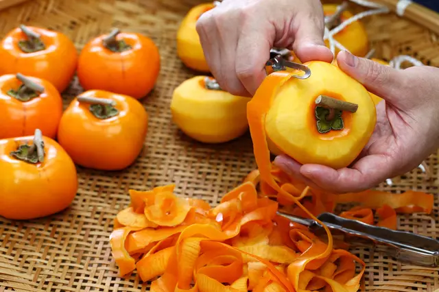 Ruční škrabání slupky z dozrálého oranžového kakeho na bambusové podložce.