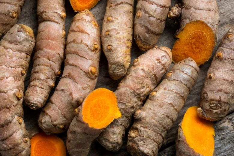 Čerstvé kořeny kurkumy s jasně oranžovým vnitřkem na dřevěném povrchu.