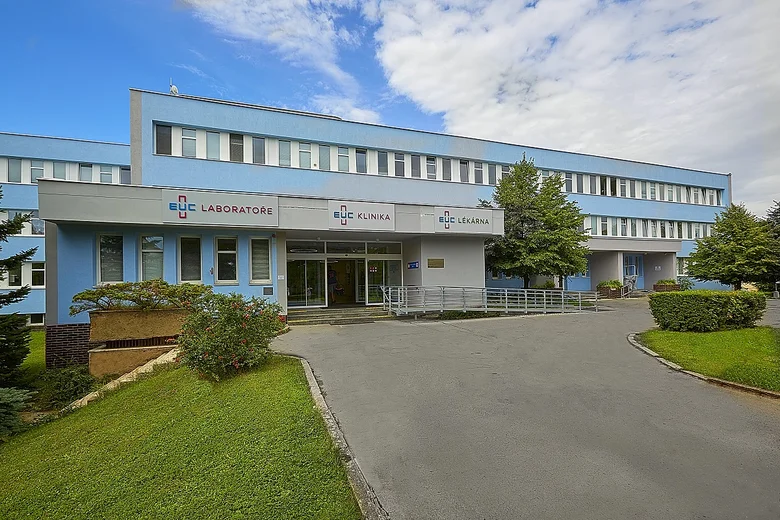 Modrá budova zdravotnického zařízení s vstupem a zelenou zahradou.