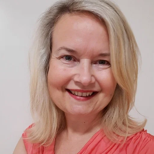 Usměvavá žena s blond vlasy v oranžovém tričku na neutrálním pozadí.