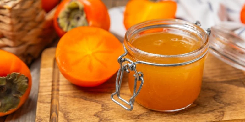 Kaki plody s rozkrojeným ovocem vedle sklenice marmelády.