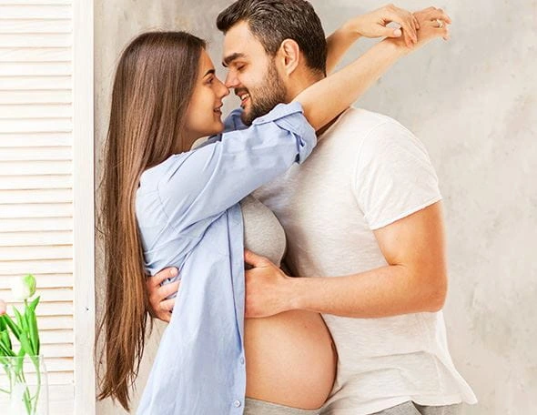 Těhotná žena objímá svého muže v intimitní poloze.