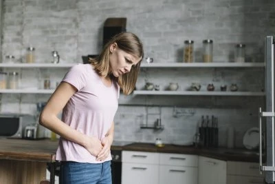 Žena v kuchyni drží břicho kvůli bolesti pod žebrem.