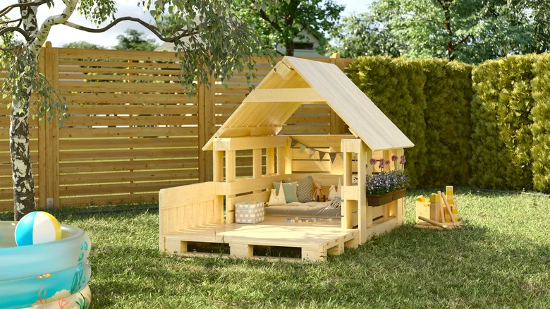 Dřevěný hrací domek z palet na trávníku s nafukovacím bazénem.