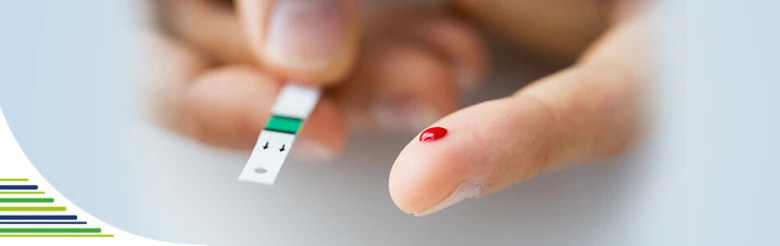 Ruka drží glukometr s kapičkou krve na prstu pro měření glykémie.
