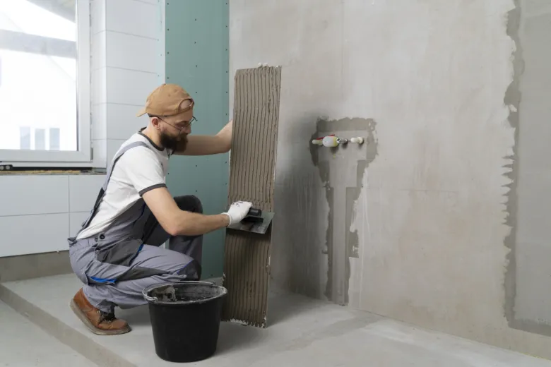 Muž nanáší lepidlo na dlaždici pro hydroizolaci koupelny.