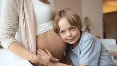 Těhotná žena s břichem drženým rukou dítěte.