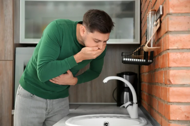 Muž zvrací do kuchyňské dřezu v zeleném tričku.