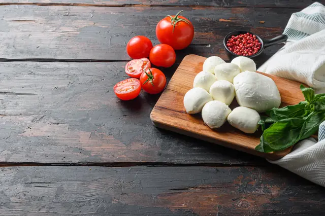 Čerstvá mozzarella s rajčaty a bazalkou na dřevěném prknu.