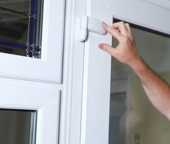 Ruka upravuje bílý plastový kování dveří.
