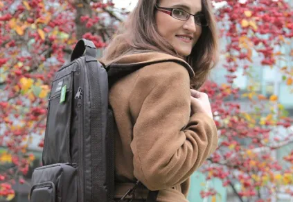 Žena s batohem venku mezi podzimními listy.