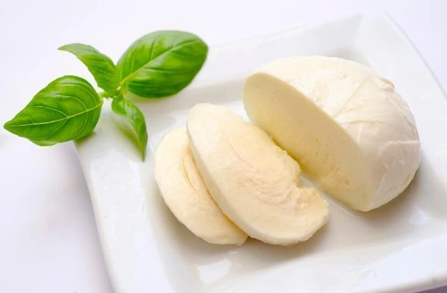 Sýr Mozzarella s čerstvými listy bazalky na bílém talíři.