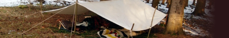 Bílá plachta vázaná mezi stromy s viditelnými dráty pro napnutí.