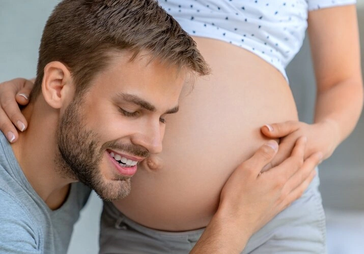 Muž dotýká břicha těhotné ženy s úsměvem.