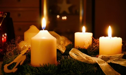 Zapálené svíčky na zeleném adventním věnci s zlatou stužkou.
