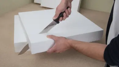 Muž řezá bílý polystyrén nožem na pracovní ploše.