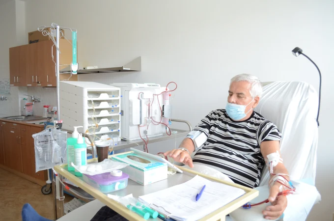 Starší pacient připojený k dialyzačnímu zařízení v nemocničním pokoji.