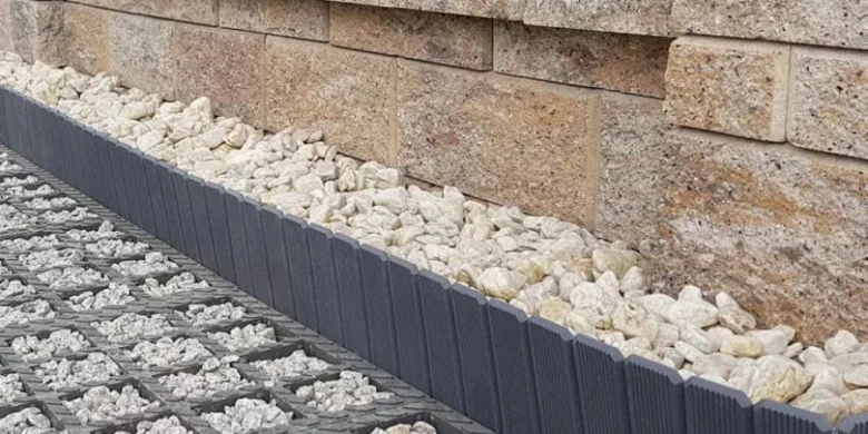 Detail základy opěrné zdi s kamínky a plastovými lištami.