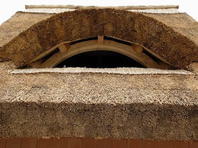 Detail doškové střechy s obloukovým oknem z dřeva.