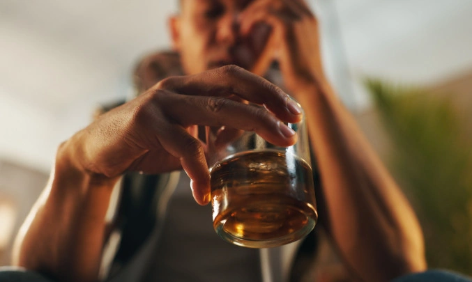 Muž drží sklenici s alkoholem v ruce.
